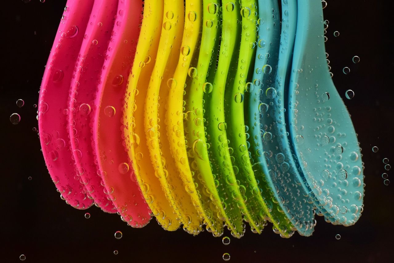 Vibrant multi-colored plastic spoons submerged in water with bubbles, creating a bright and playful image.